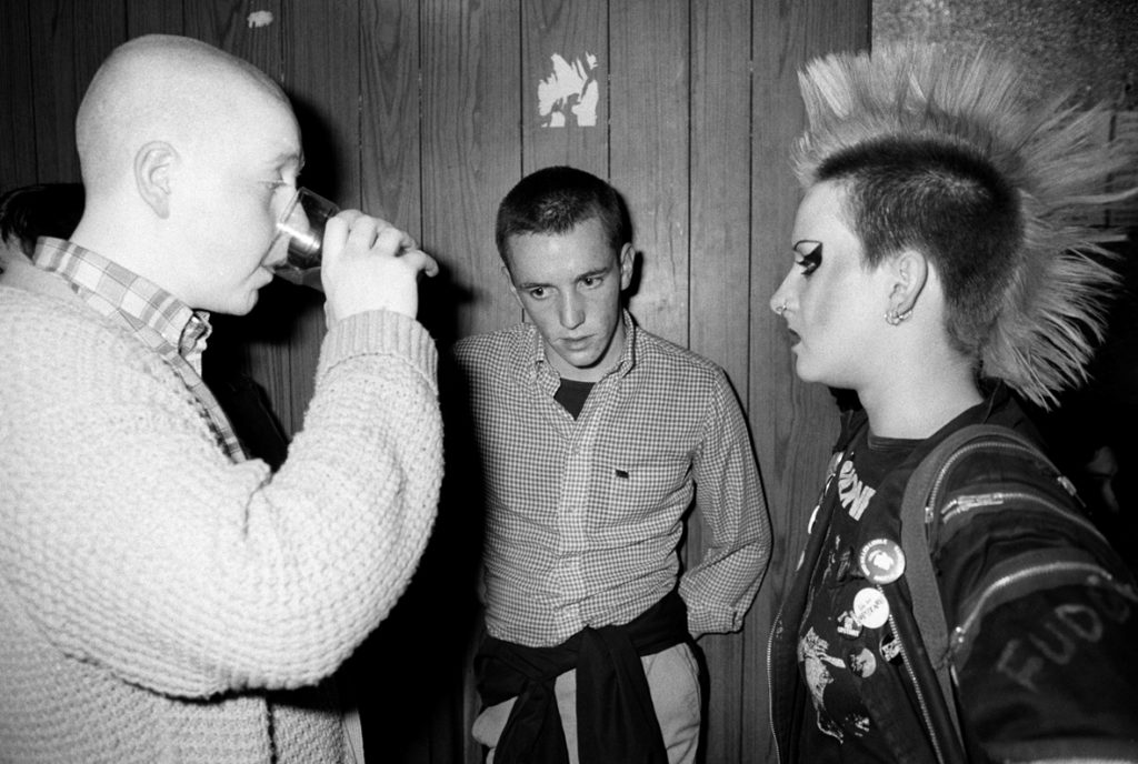 Un skinhead, un suedehead et une punk prenant un verre à l’étage de l’Electric Ballroom, Camden Town, Londres, 1980. © Homer Sykes